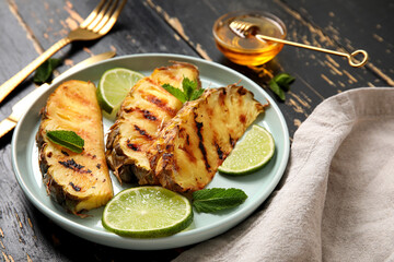 Plate with grilled pineapple slices and lime on dark wooden background, closeup