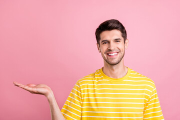 Portrait of attractive cheerful guy holding on palm copy space ad promo offer isolated over pink pastel color background © deagreez