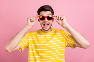 Portrait of attractive amazed cheerful guy wearing touching specs having fun isolated over pink...
