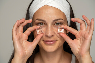 portrait of a young woman holding ice cubes under her eyes