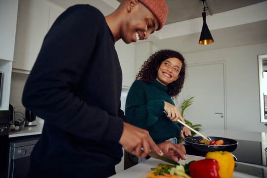 Young Mixed Race Couple Cooking Food In The Kitchen At Home. Happy Couple Preparing Food And Smiling. High Quality Photo 