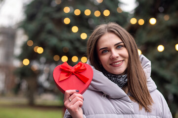 Merry woman holding girt box at the street with Christmas decoration