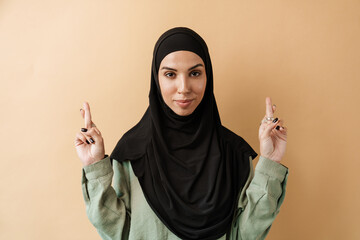 A portrait of the positive muslim woman with pierced nose in hijab hoping for something with crossed fingers