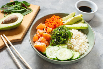 Salmon poke with avocado, seaweed, pickled carrots and cucumber on concrete table