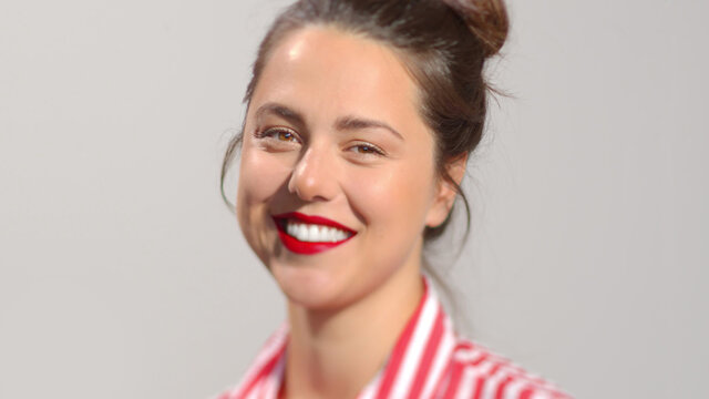 Young attractive dark hair female with vivid red lipstick photo portrait. A lady with brown hair in a bun smiles looking to the camera wide smile showing perfect white teeth. Close-up studio shot 