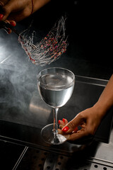 Great view of glass with drink that female bartender decorates by caramel with flower petals