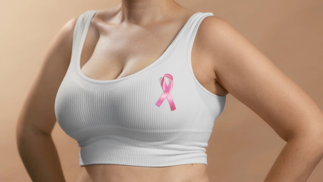 Young lady in a white top with a ribbon sign on her chest to support pink October and females combating breast cancer. Anonymous studio shot photo on beige background.