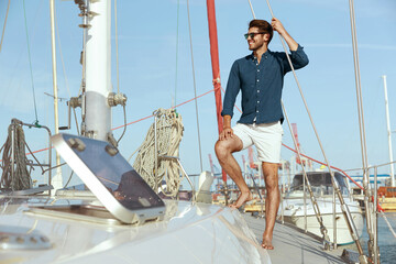 Young man standing on board of his yacht in harbor