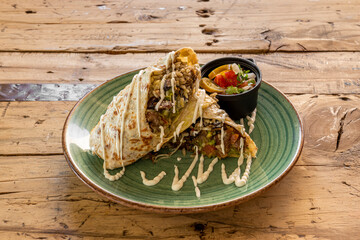 Mexican wheat tortilla burrito with pico de gallo, rice, cream cheese, jalapenos and chili con carne on wooden table