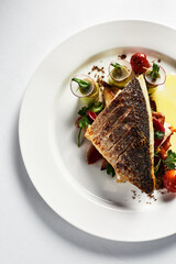 Grilled sea bass with fried tomatoes, served with potatoes. Fish dish top view, light background, copy space