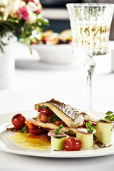 grilled sea bass with sauteed tomatoes, served with a potato ball on a white plate, sea bass fillet outline on a light background