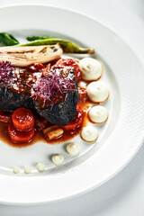 Braised beef cheeks with vegetables, cooking beef cheeks in red wine sauce with fried spinach leaves and carrots on light background top view