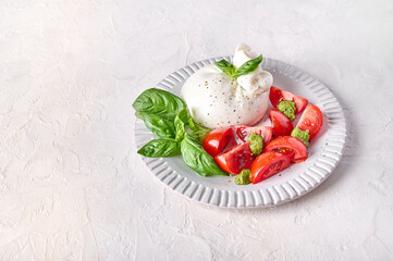 Traditional italian burrata cheese with basil and tomato on light background. Close up