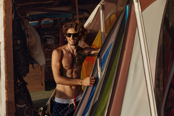 Surfer stand in wooden hut with surf equipment