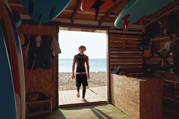 Obraz na płótnie Canvas Surfer entering to wooden hut on sandy beach