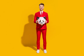 Photo of cheerful handsome blond guy hold panda mask wear red tuxedo tie isolated on yellow color background © deagreez