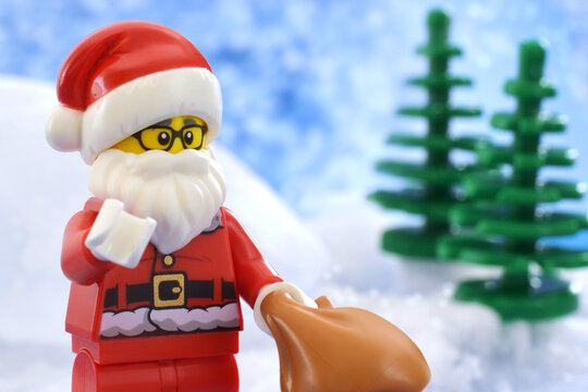Editorial illustrative image of lego minifigure Santa Claus on white snowing background with green christmas trees. 