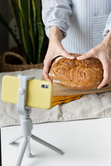 a woman baker tells a bread recipe online, a culinary blog, video cooking courses about baking bread, a food photographer, women's hands hold bread against the background of a light apron, bread with