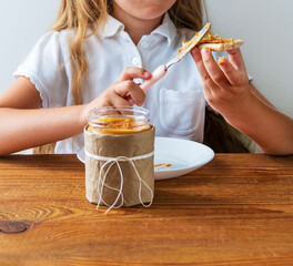 Child spreading peanut butter on crispbread eating sandwich wooden table home kitchen.School girl...