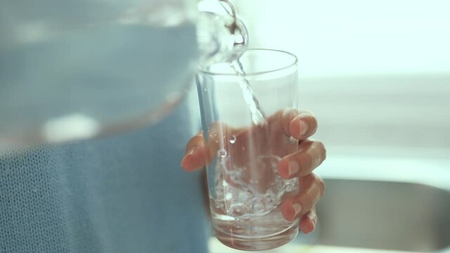 Closeup woman hands pouring water into glass from bottle. Slow motion.