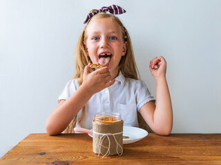 Child eating crispbread with peanut butter sitting at table home kitchen. School girl with bread...