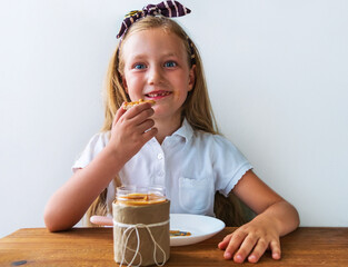 Child eating crispbread with peanut butter sitting at table home kitchen. School girl with bread...