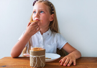 Child eating crispbread with peanut butter sitting at table home kitchen. School girl with bread...
