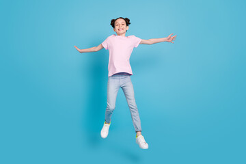 Photo of charming pretty school girl wear pink t-shirt smiling jumping high arms sides isolated blue color background