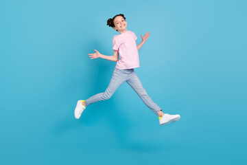 Fototapeta na wymiar Photo of pretty funky school girl wear pink t-shirt smiling jumping high arms sides isolated blue color background