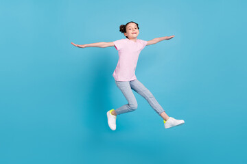 Fototapeta na wymiar Photo of funny charming schoolgirl dressed pink t-shirt arms sides jumping high smiling isolated blue color background
