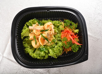 stir fried big tiger prawn with salted egg yolk creamy sauce and curry leaf in black party bento tray box for asian take away halal menu