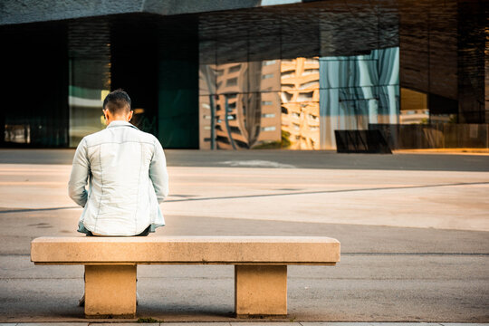 Young Caucasian Man Sitting Backwards On A Bench.