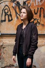 Naklejka na ściany i meble A brunette girl with a bob haircut in a black windbreaker stands in front of a textured wall