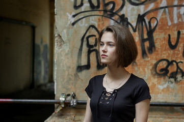 A brunette girl with a bob haircut in a black t-shirt stands in front of a textured wall 