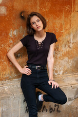 A brunette girl with a bob haircut in a black t-shirt stands in front of a textured wall 