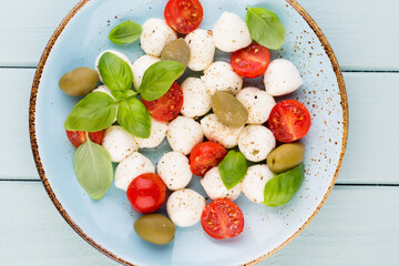 Delicious caprese salad with ripe cherry tomatoes and mini mozzarella cheese balls with fresh basil leaves.