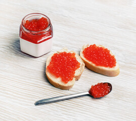 Delicious red caviar, sandwiches with caviar, glass jar and spoon on light wooden background.