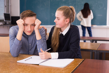 Worried teen girl comforting sad coursemate having learning difficulties in class