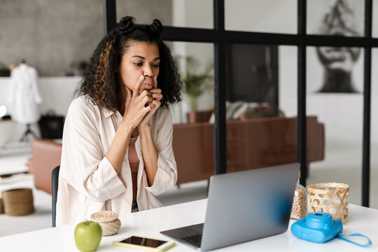 Black young woman doing facial massage while using laptop at home
