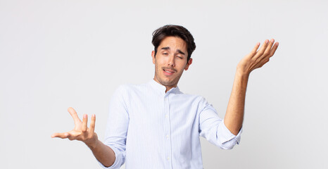 hispanic handsome man shrugging with a dumb, crazy, confused, puzzled expression, feeling annoyed...