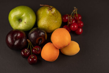 Fresh fruits and dried fruit powder. Pear, apple, apricot, cherry, currant, strawberry and plum on dark paper background. Vegetarian healthy detox food.