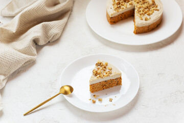 Slice of carrot cake with coconut cream and walnuts on a white plate. Raw cake, no baked goods. Sugar, gluten and lactose free.