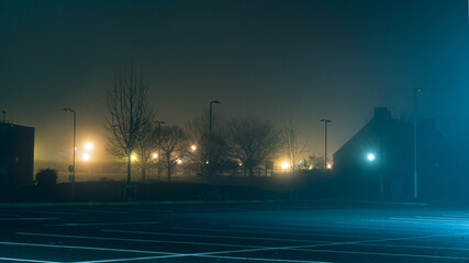 An empty car park with street lights glowing in the distance on a mysterious moody,  foggy...