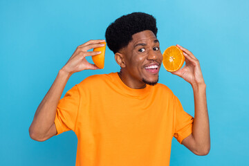 Photo of young happy dark skin man hold hands orange slices vitamins smile isolated on blue color background