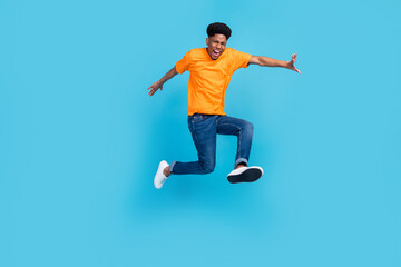 Fototapeta na wymiar Full length photo of impressed brunet millennial guy jump yell wear orange t-shirt jeans isolated on blue color background