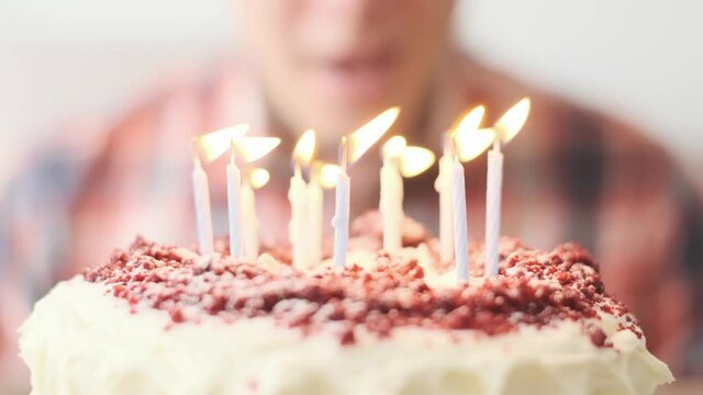 Unrecognizable man blows out the candles on a birthday cake. Close-up. Selective focus on cake and candles.