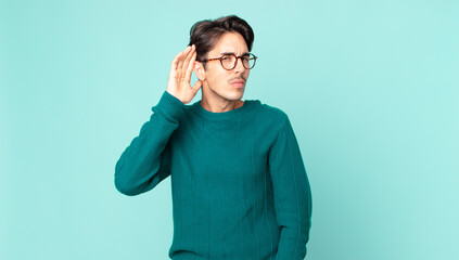 hispanic handsome man looking serious and curious, listening, trying to hear a secret conversation...