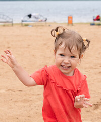 Emotional child plays in the sand by the sea. Happy eyes of a child running by the pond. The girl runs and looks into the frame on the beach.