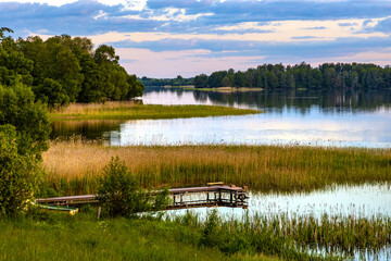 Panoramic summer view of Jezioro Selmet Wielki lake landscape with vintage pier reeds and wooded shoreline in Sedki village in Masuria region of Poland - obrazy, fototapety, plakaty