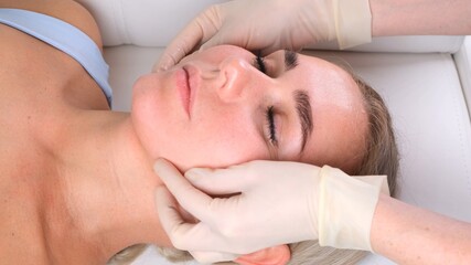 Fototapeta na wymiar Facial massage beauty treatment. Close up of a young womans face lying on back, getting face lifting massage, pinch and roll technique